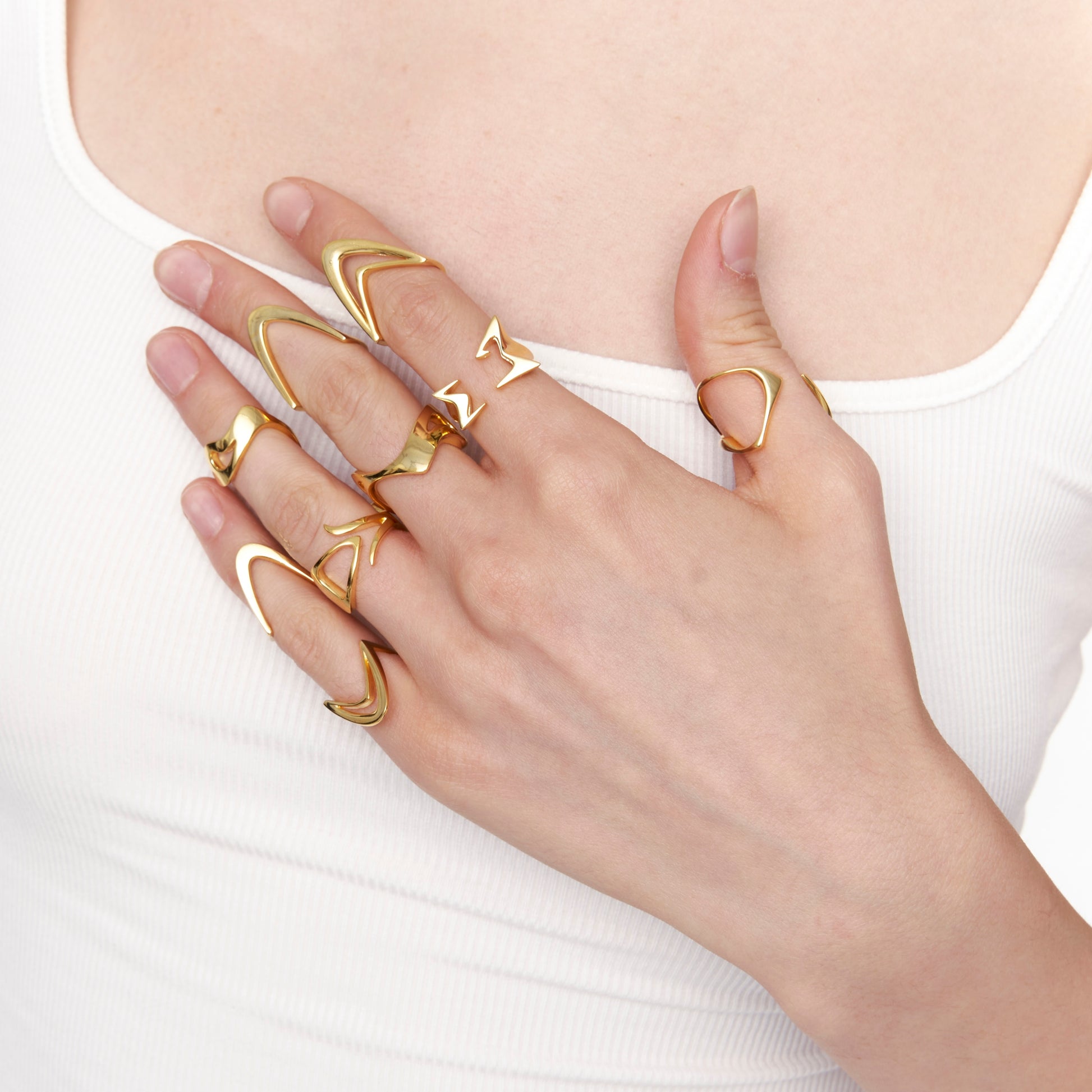 Model’s hand wearing stacked gold rings in sculptural, modern shapes on white top