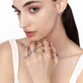 Female model showcasing layered sculptural silver rings in bold geometric shapes, styled with slicked-back hair and white tank for a minimalist, futuristic editorial look.