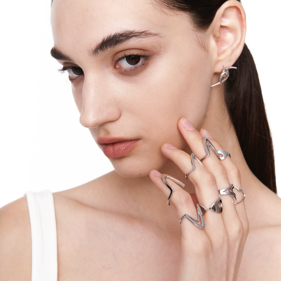 Female model wearing the Sharp Curve Ring in silver, styled with multiple sculptural rings to highlight its futuristic and edgy design.