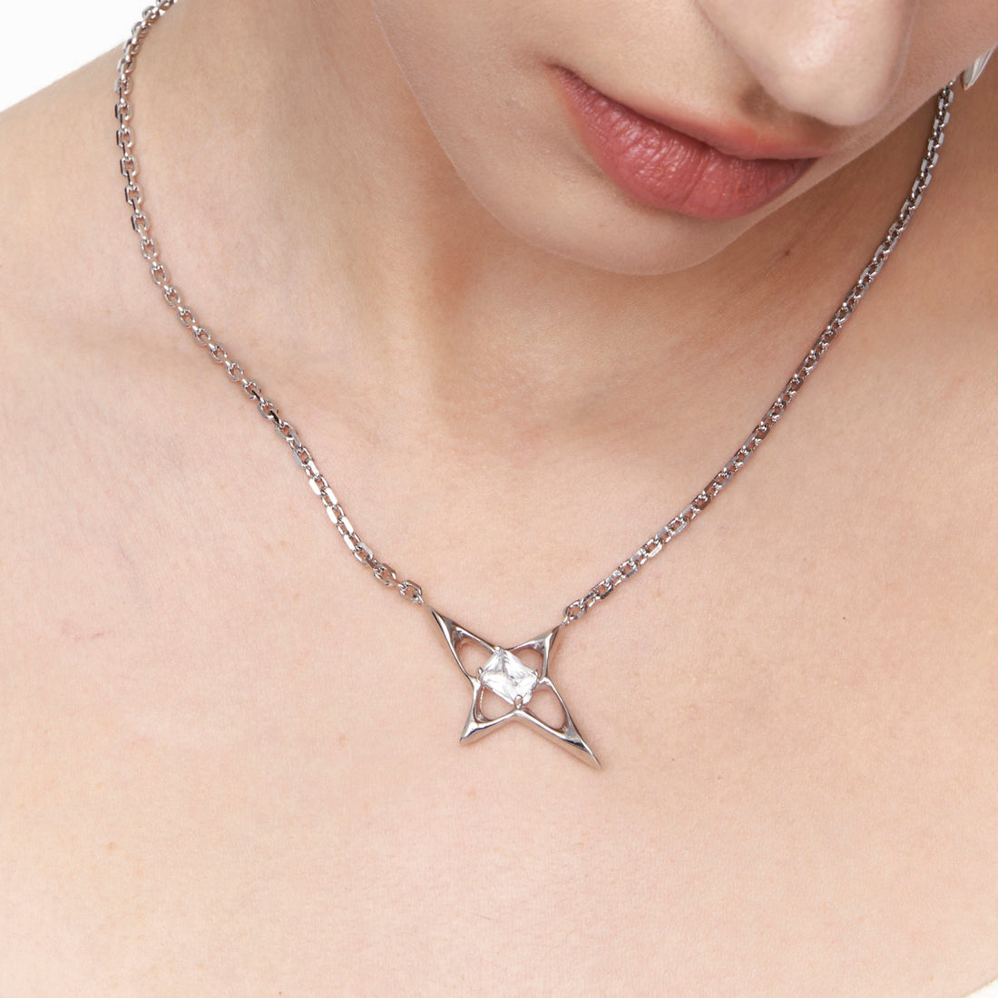 Close-up of a silver geometric star necklace with faceted center stone on a high-shine chain. Sculptural 925 sterling silver pendant with futuristic Y3K design.