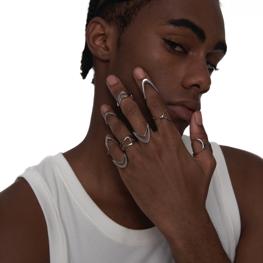 Model wearing stacked sculptural silver rings on multiple fingers, featuring an open V-shape design