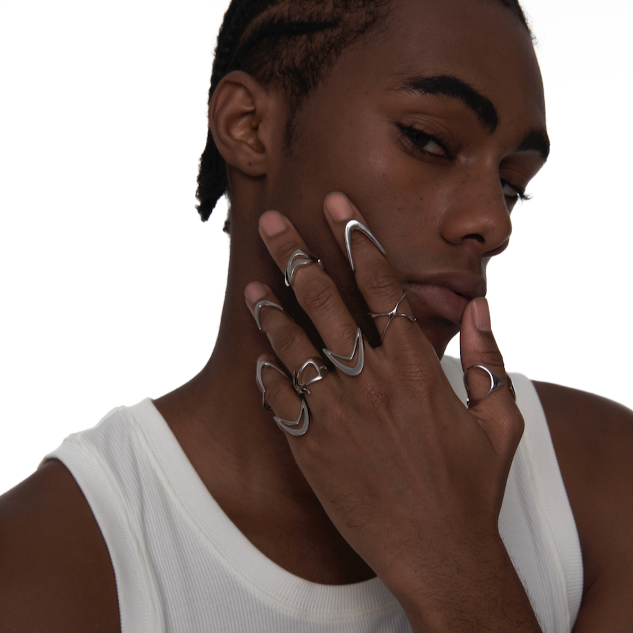 Male model wearing silver Double-Arc Ring stacked on multiple fingers, styled with other sculptural rings in a cyberpunk look


