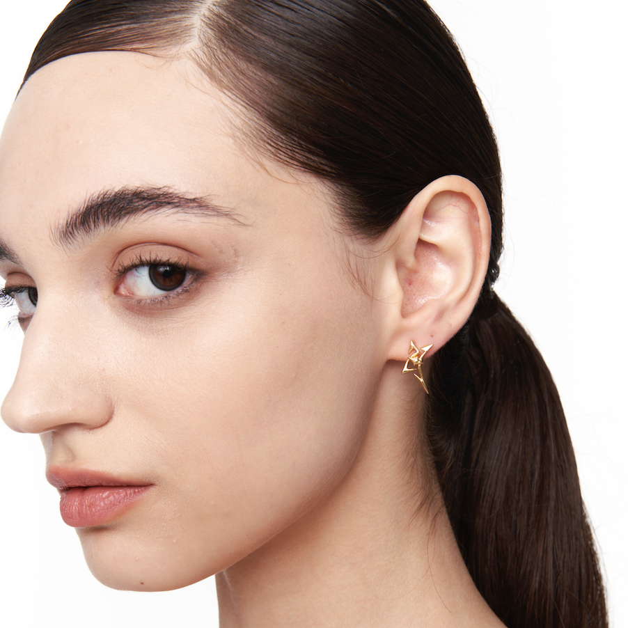 Side profile of female model wearing gold spike-shaped star earring with sharp angular design; unisex futuristic jewelry for everyday edge