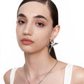 Close-up of model wearing angular silver earring with star-shaped design and clear crystal, styled with sleek hair and a white tank top against white background.








