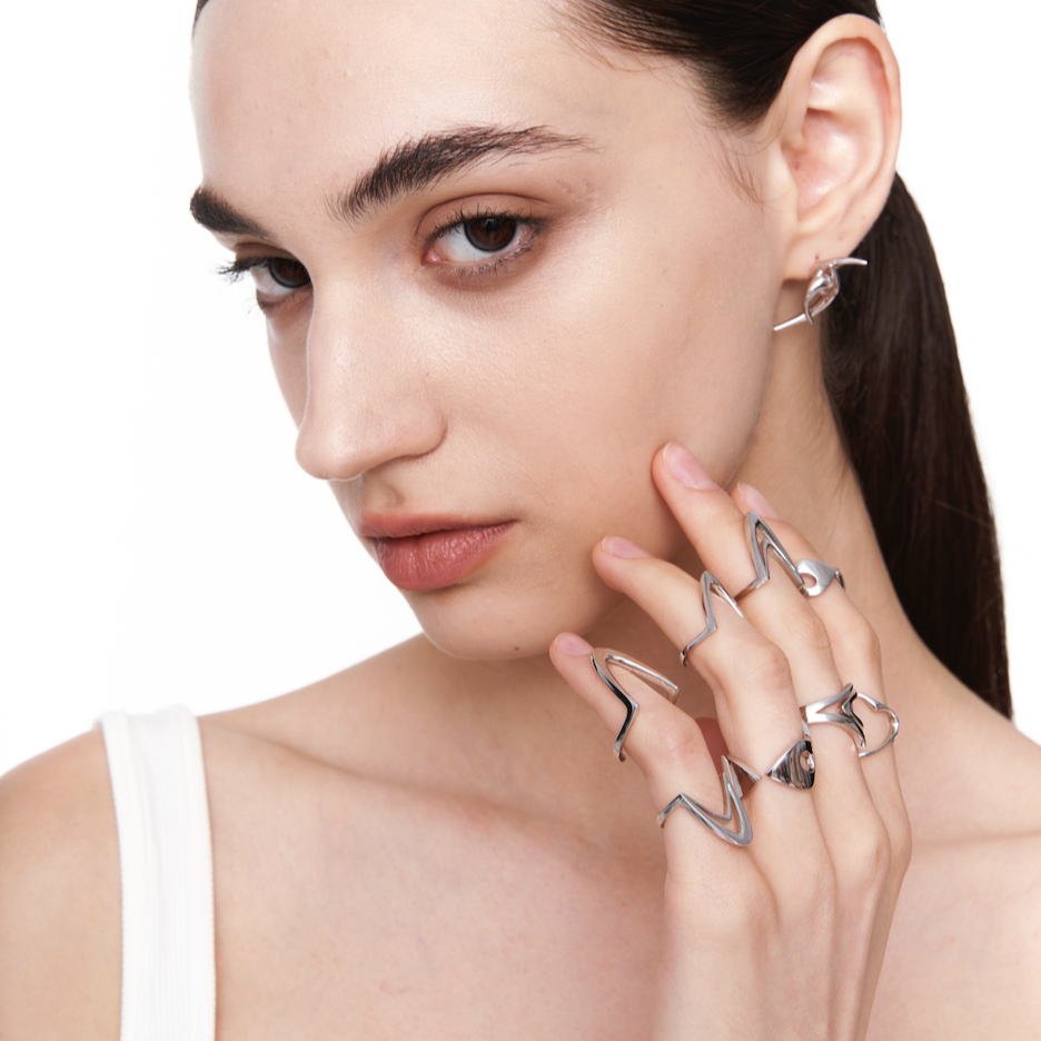 Model wearing stacked geometric silver rings on fingers with sleek hairstyle and minimal white top, showcasing an expressive cyber-inspired look

