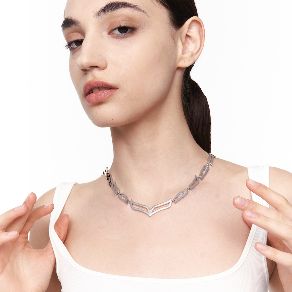 Model adjusting My Heart Soars silver V-link necklace, a chunky sculptural chain resting above the collarbone