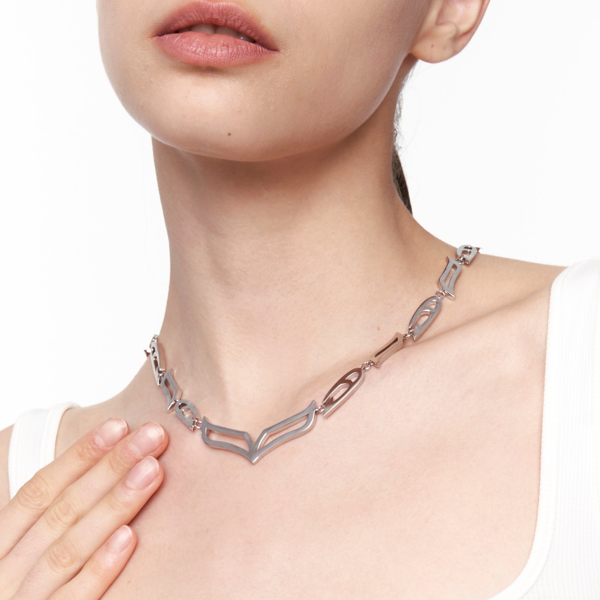 Model wearing the My Heart Soars silver necklace with V-shaped centerpiece and sculptural links, styled over a white tank top.