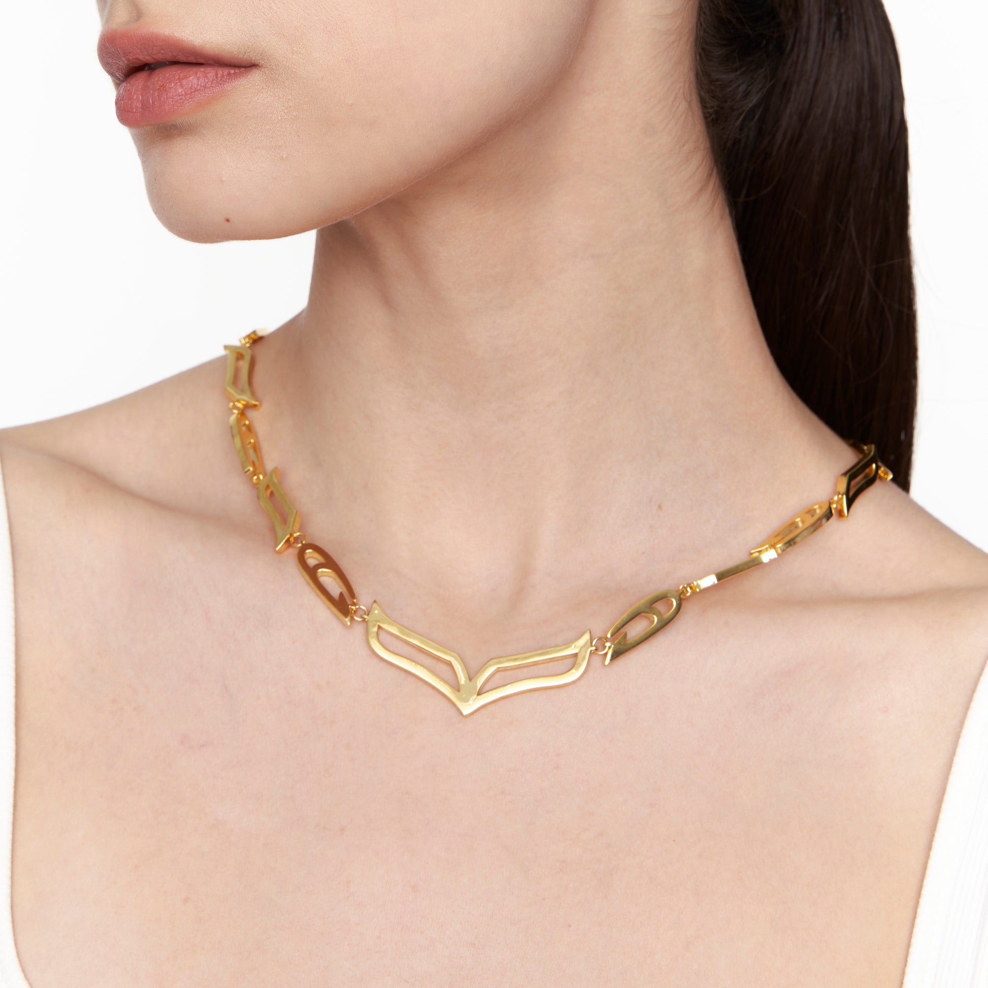 Model wearing the My Heart Soars gold necklace with sculptural wing-inspired links and a bold V-shaped centerpiece, styled against a white background.