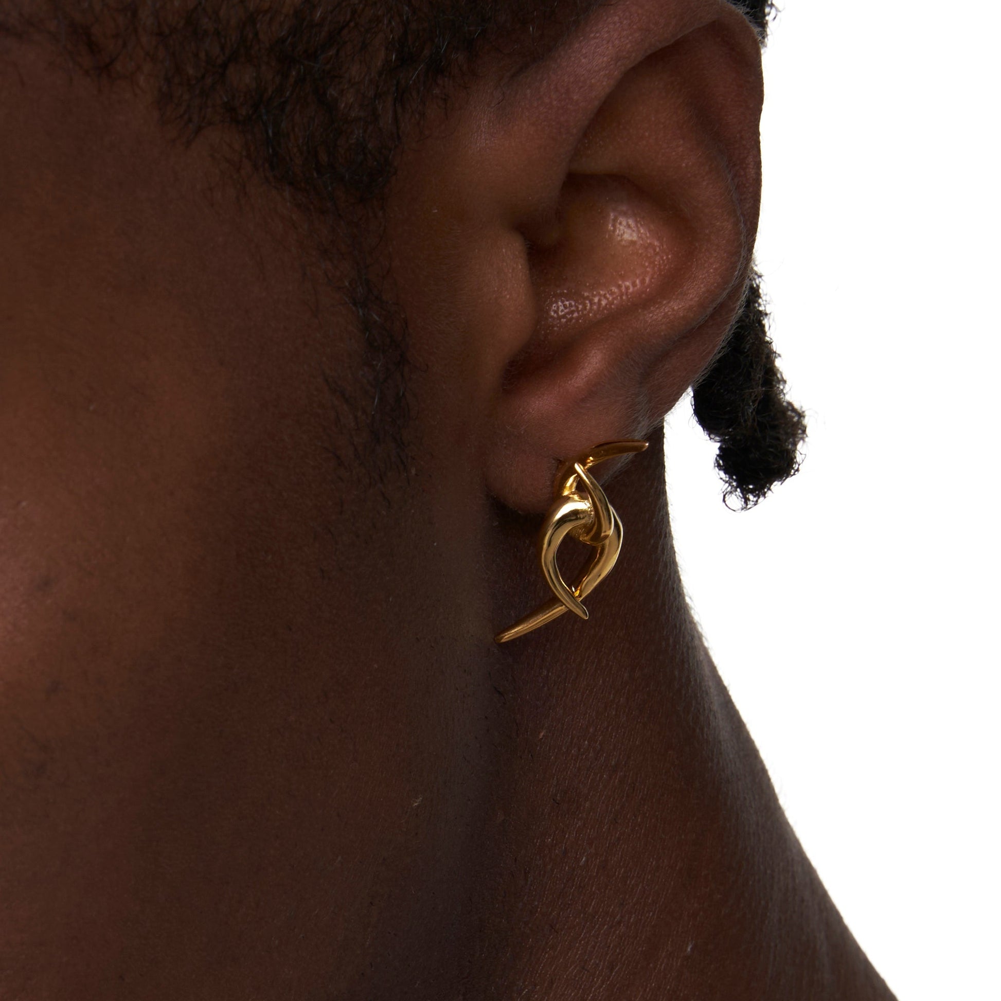 Close-up of a gold sculptural Neural Link earring worn on ear, featuring a curved, futuristic design from Outsider Artist.