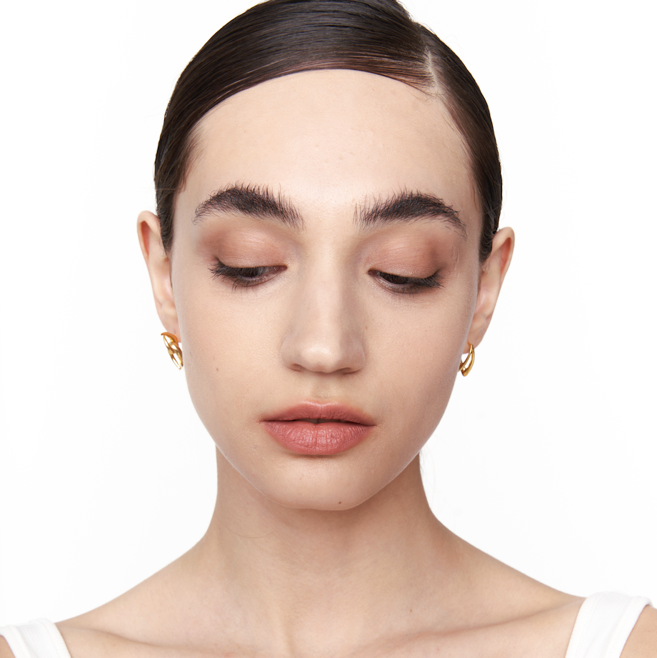 Model wearing Neural Link gold sculptural earrings, front-facing view with eyes closed