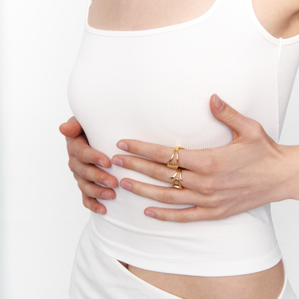 Model wearing stacked Outsider Artist rings in polished 18k gold, featuring abstract open-form designs on index and middle fingers.