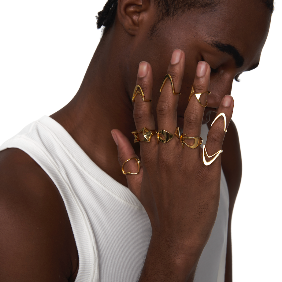 Male model with hand over face wearing stacked gold rings crafted from recycled sterling silver with 18k gold plating, styled in a white ribbed tank for a bold, sculptural editorial look.