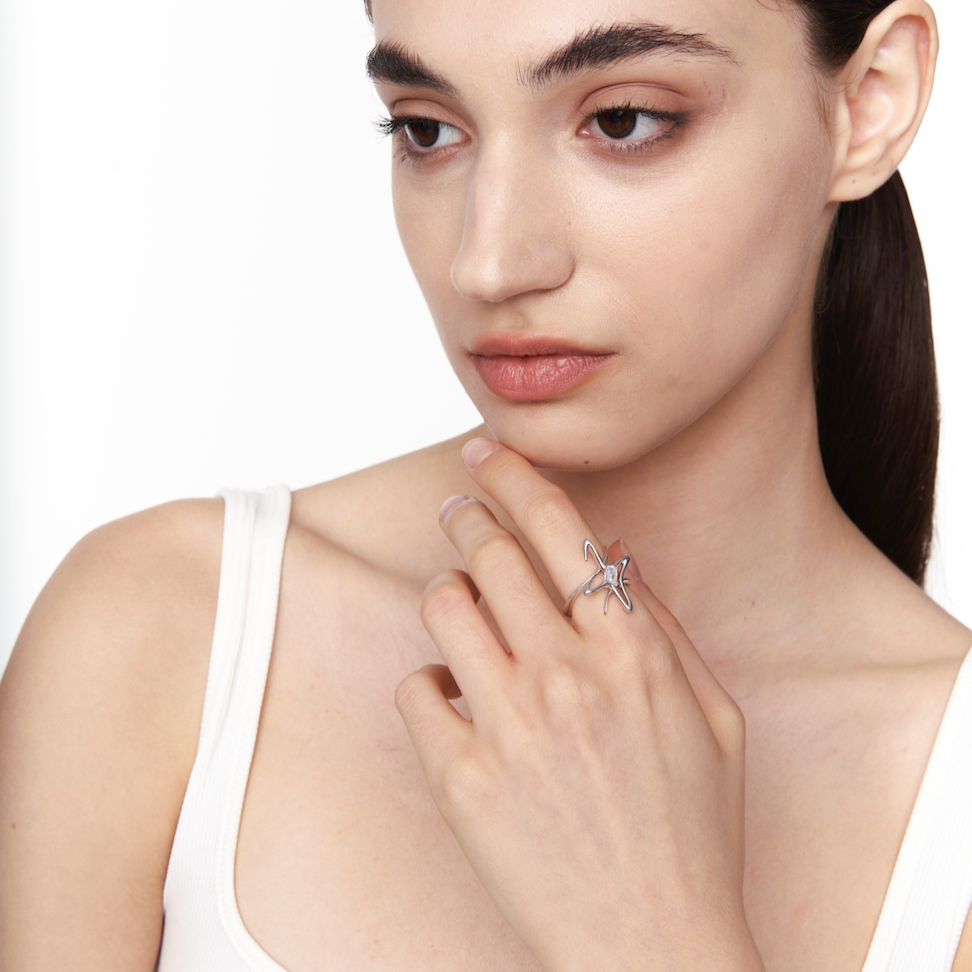 Model wearing a sculptural silver star ring with a central crystal, styled on the index finger for a sleek, futuristic look.