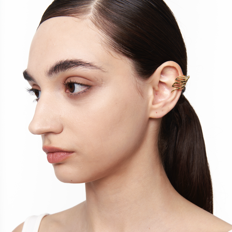 Gold aerodynamic ear cuff styled on model’s ear from side angle, no piercing required